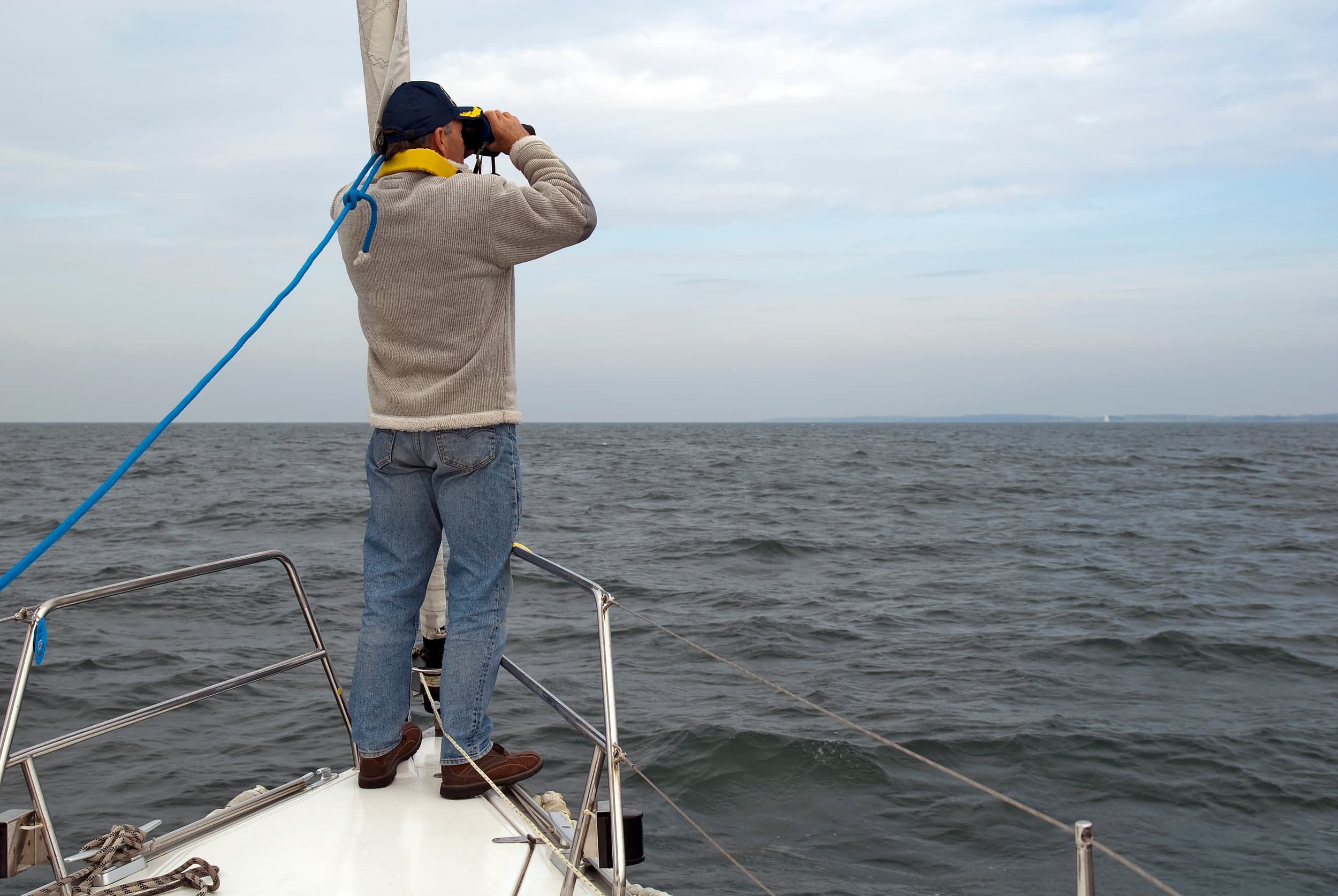 Mann mit Fernglas steht konzentriert am Bug einer Segelyacht und blickt auf das offene Meer – Symbol für Abenteuer und Navigation beim Skippertraining in Kroatien.