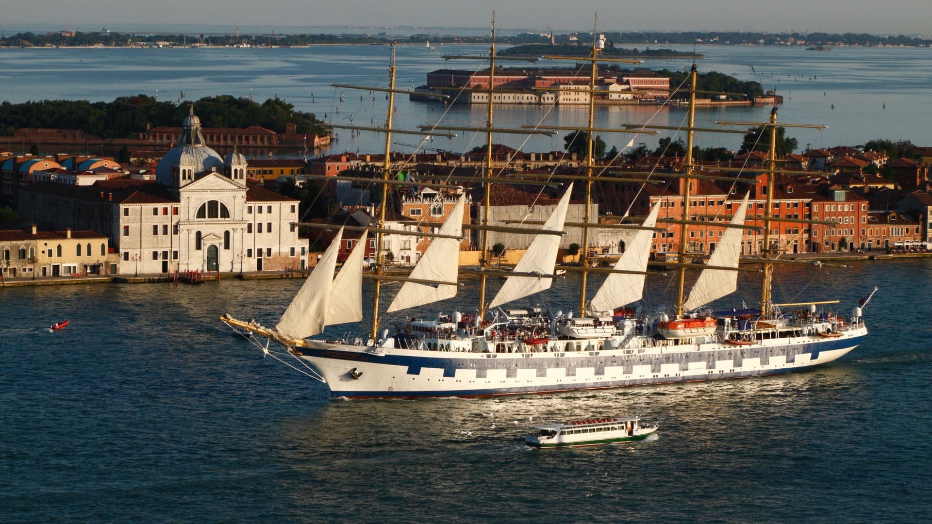 Elegantes Segelkreuzfahrtschiff mit weißen Segeln in der Lagune von Venedig, im Hintergrund die historische Stadtkulisse mit der Kirche San Giorgio Maggiore