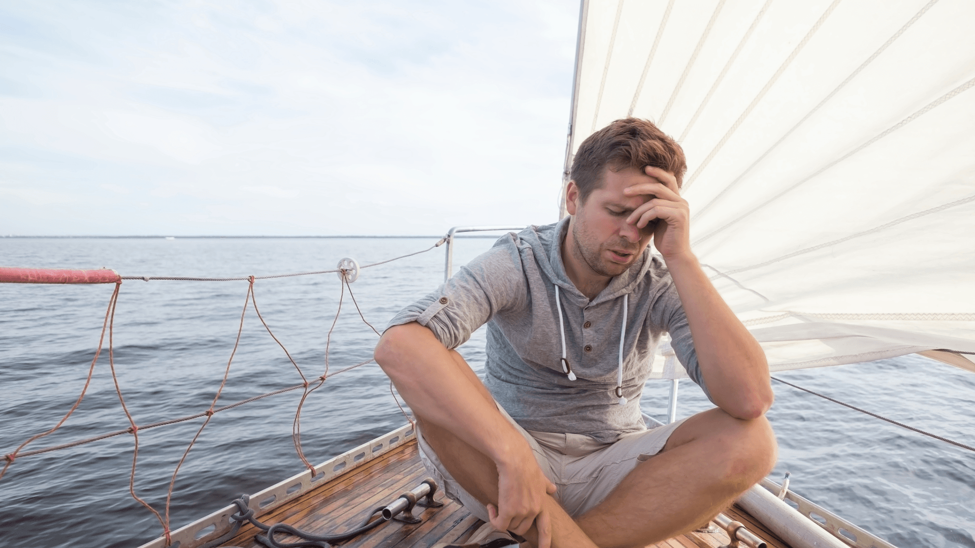 Mann sitzt vorn am Bug einer Segelyacht und kämpft gegen Übelkeit