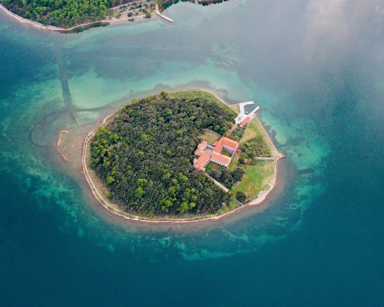 Luftaufnahme der kleinen Insel Košljun bei Krk mit Klosteranlage, umgeben von türkisfarbenem Wasser