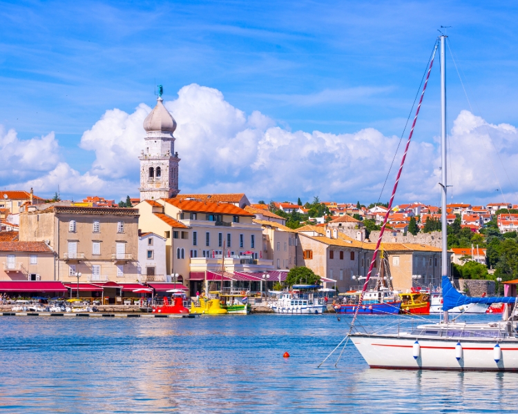 Blick auf die Altstadt von Krk mit Hafen, Booten und dem markanten Glockenturm vor blauem Himmel
