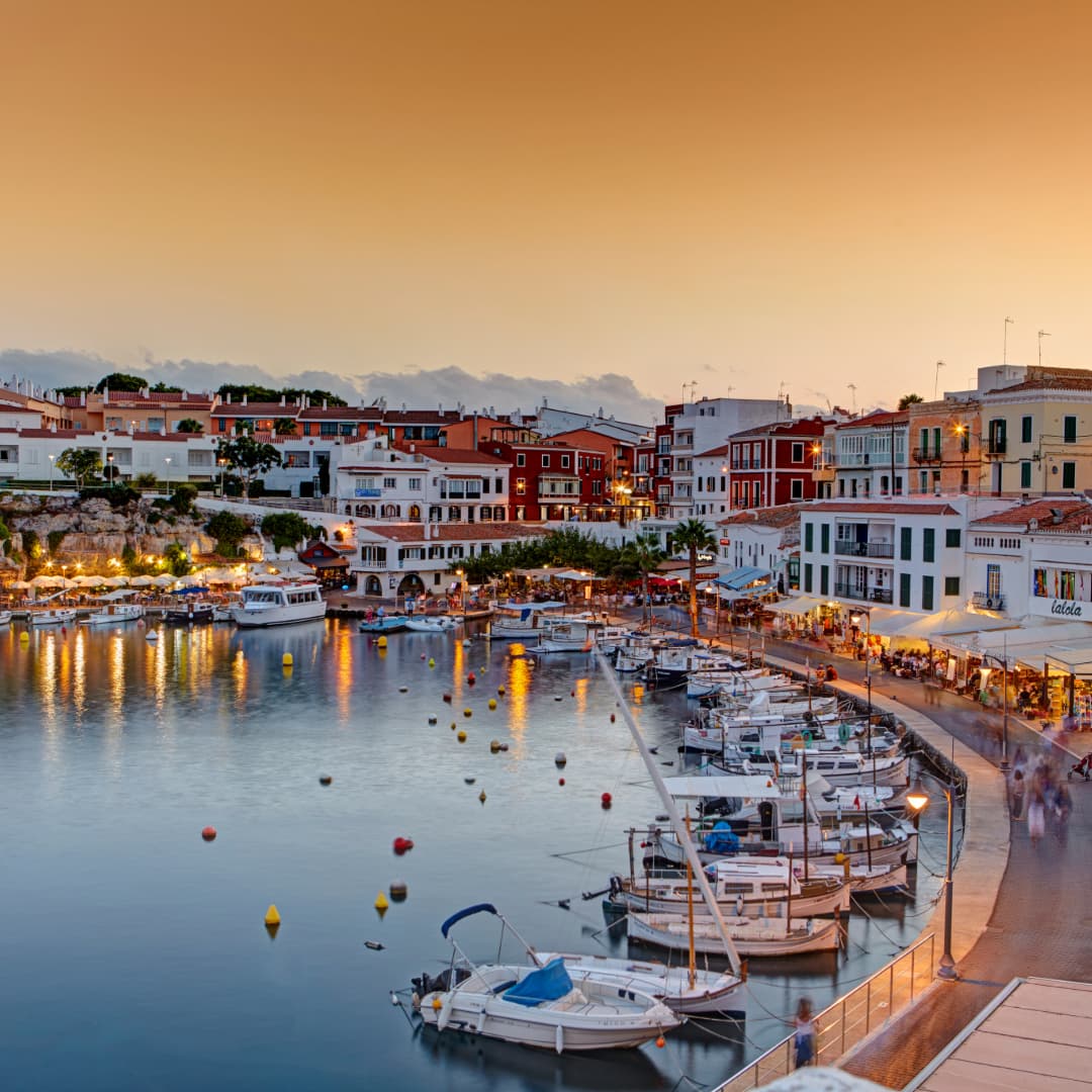 Romantischer Blick auf den beleuchteten Hafen von Mahon auf Menorca während des Sonnenuntergangs – ideales Ziel für Segeltörns auf den Balearen