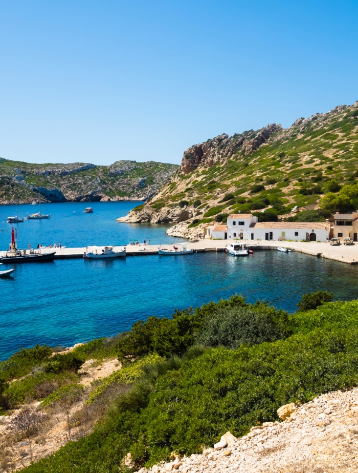Blick auf den Hauptkai von Cabrera im Nationalpark mit Fischerhäusern, Anlegestelle und Segelbooten im Hintergrund – exklusives Segelziel mit BlackSails-Yachting.