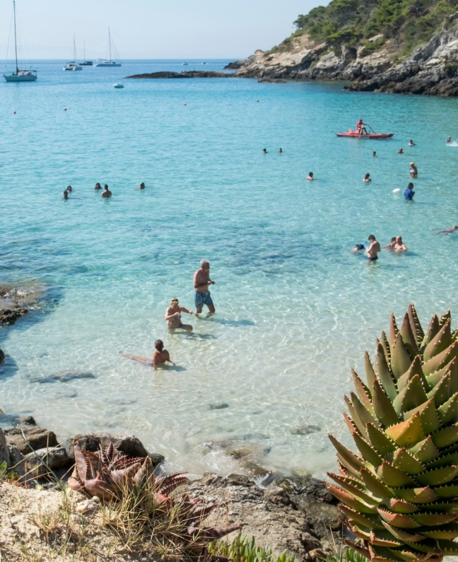 Menschen baden im türkisblauen Wasser der Bucht von Capraia, im Hintergrund segelnde Yachten – Yachtcharter mit BlackSails-Yachting im Tyrrhenischen Meer
