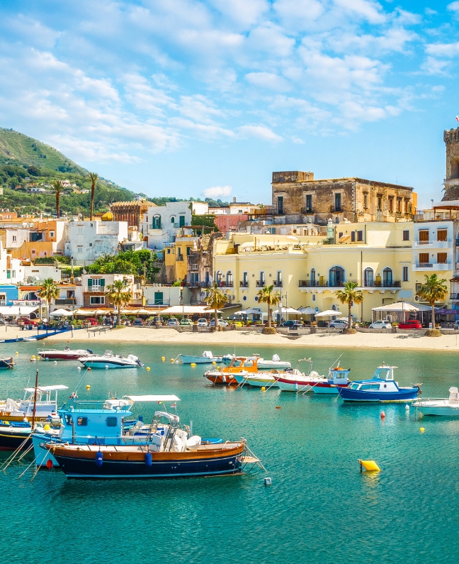 Bunte Fischerboote und historische Gebäude in einem Hafen auf Ischia – Yachtcharter mit BlackSails-Yachting im Golf von Neapel