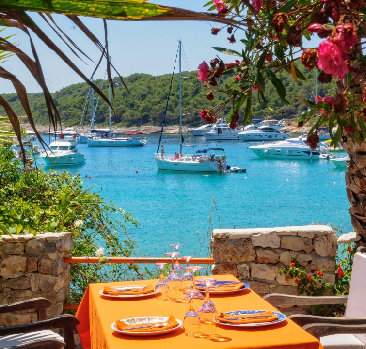 Segelyachten vor Hvar Stadt mit Restaurantterrasse und Blick auf die Bucht – Zwischenstopp beim Yachtcharter Mitteldalmatien mit BlackSails-Yachting