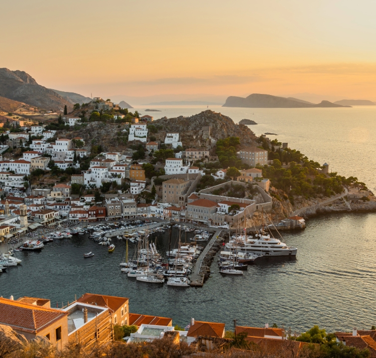Abendstimmung über dem Hafen von Hydra mit weißen Häusern und festgemachten Yachten – ein Zwischenziel beim Yachtcharter mit BlackSails-Yachting
