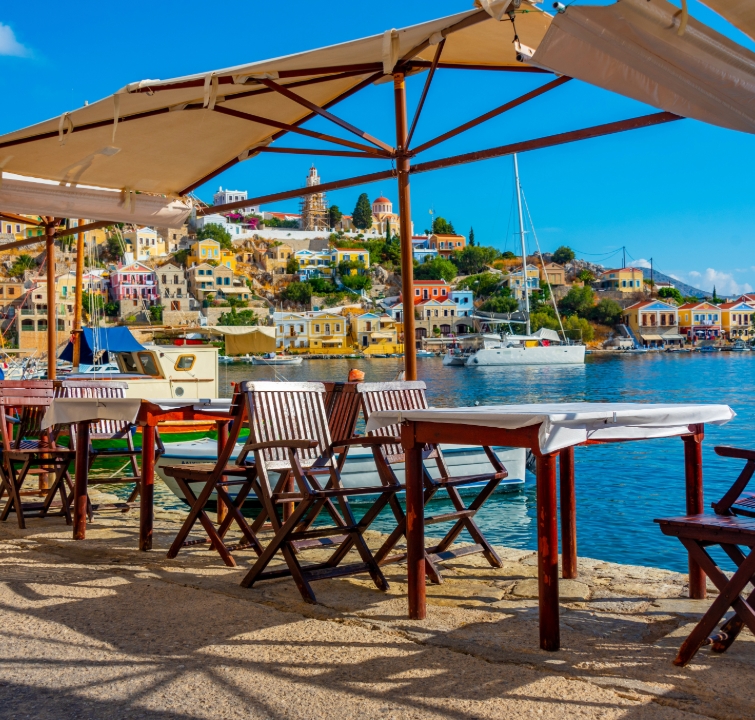Taverne mit Blick auf den farbenfrohen Hafen von Symi, Griechenland – beliebtes Ziel beim Yachtcharter mit BlackSails-Yachting im Dodekanes.