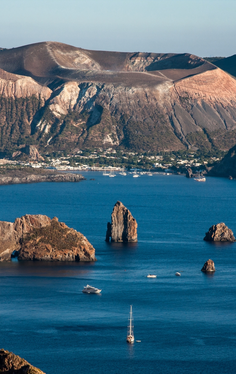Segelyachten vor der zerklüfteten Küste von Vulcano mit Blick auf den Krater – Yachtcharter mit BlackSails-Yachting