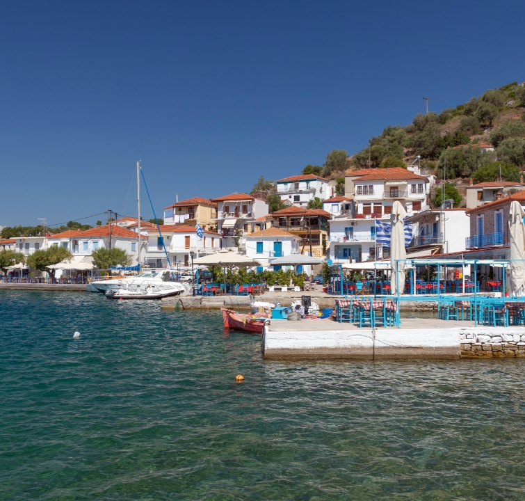 Küstenort in Griechenland mit weiß-blauen Häusern, Tavernen und anliegenden Yachten – idealer Zwischenstopp beim Yachtcharter mit BlackSails-Yachting.