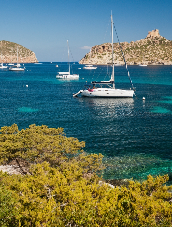 Segelyachten an Bojen im klaren Wasser der Bucht von Cabrera, im Hintergrund die historische Festung – Segeln im Nationalpark mit BlackSails-Yachting.
