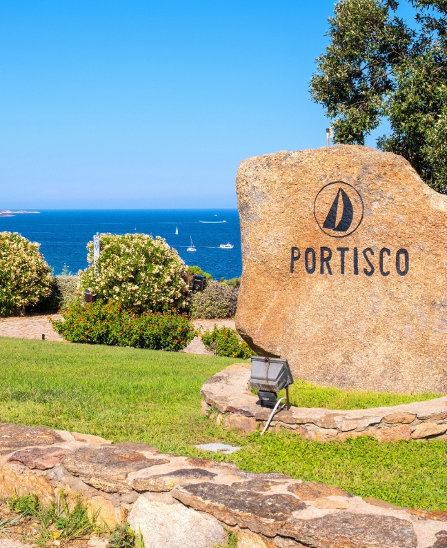 Granitstein mit der Aufschrift "Portisco" vor dem Meer mit Segelbooten – Rückkehrpunkt bei einer Yachtcharter mit BlackSails-Yachting