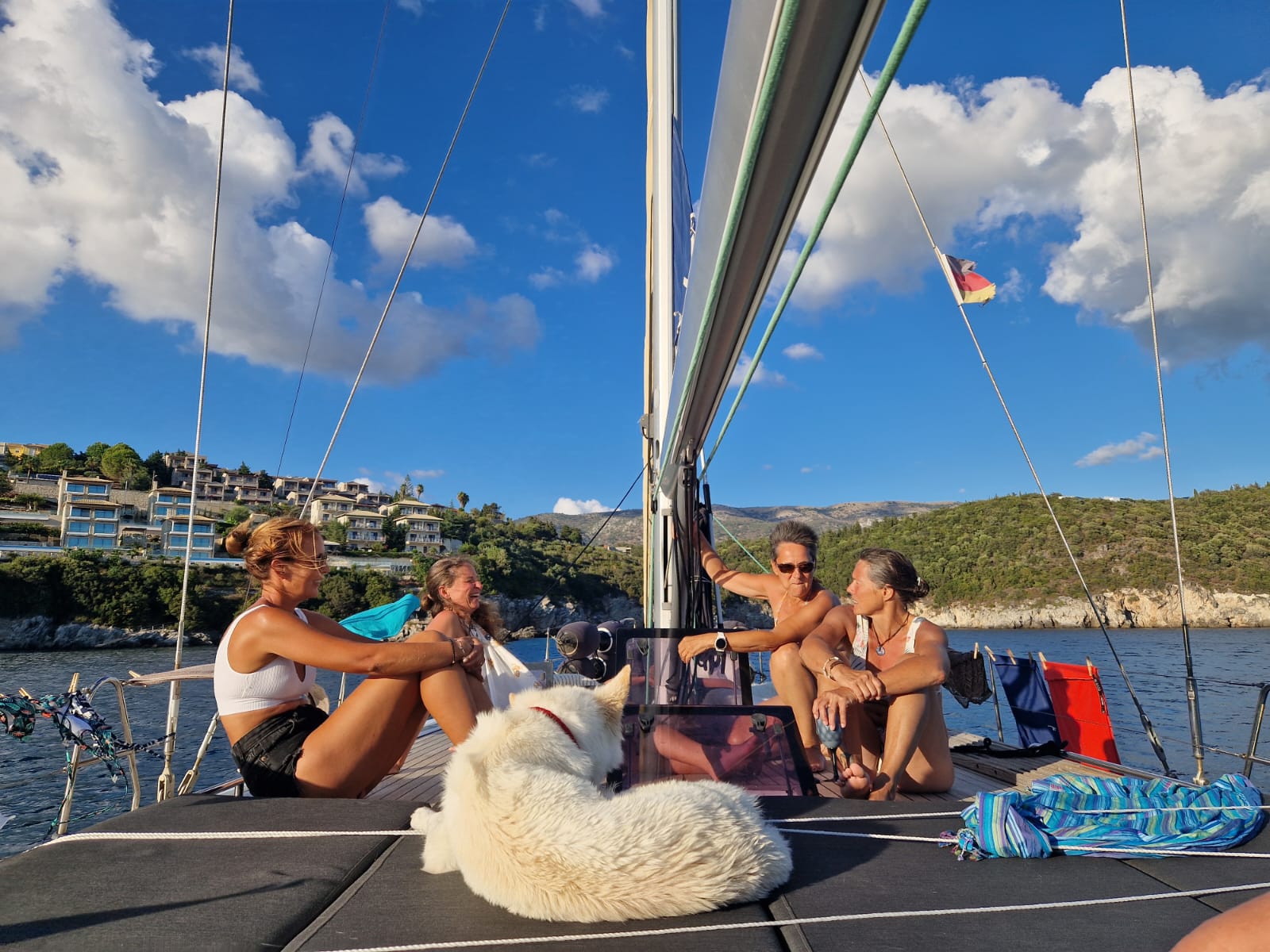 Frauen sitzen entspannt auf dem Vorschiff einer Segelyacht in Kroatien bei Sonnenschein – mit Hund an Bord und Blick aufs Ufer.