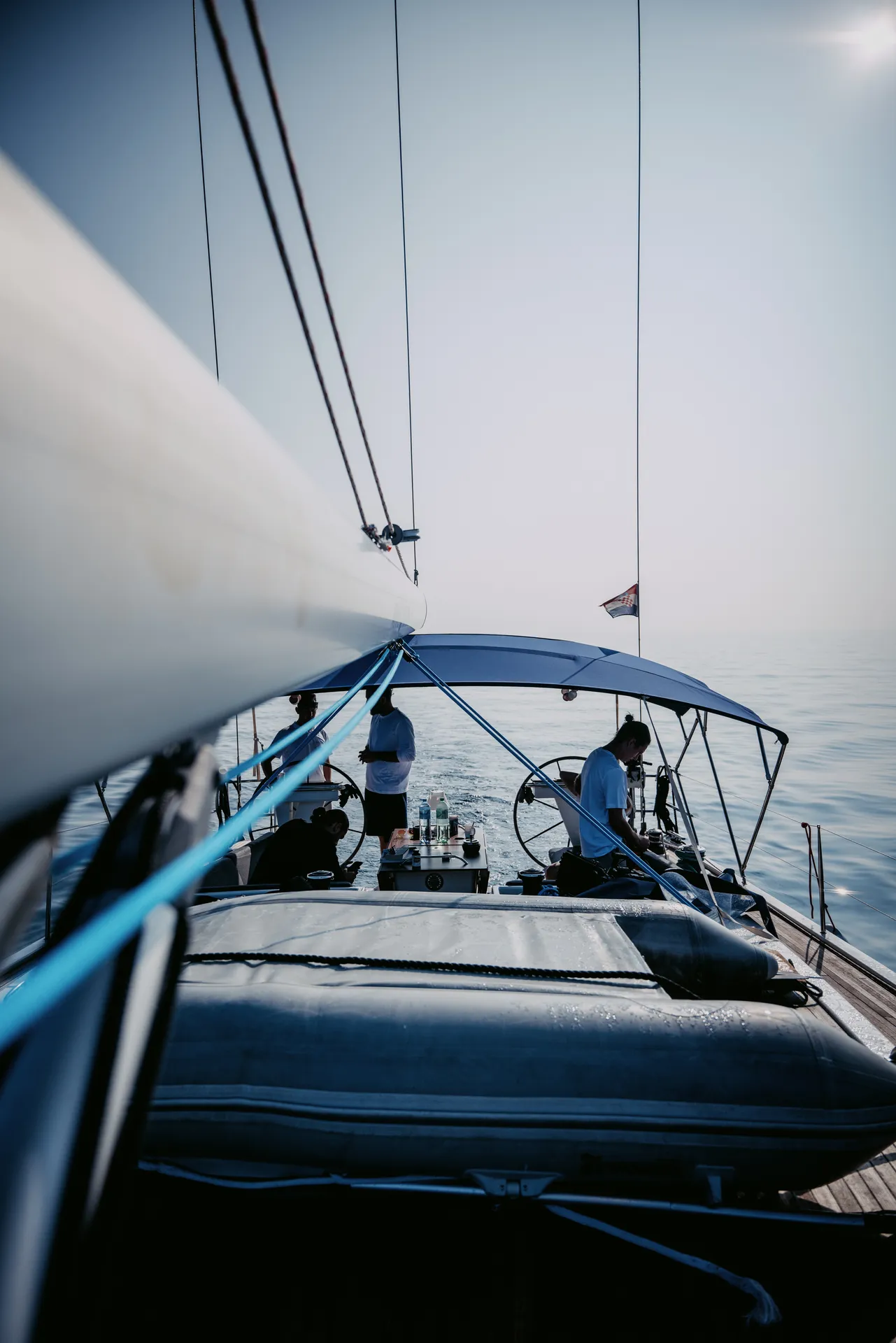 Unter Segeln: Blick am Großbaum entlang ins Cockpit, die Crew an den Steuerrädern unter dem blauen Bimini
