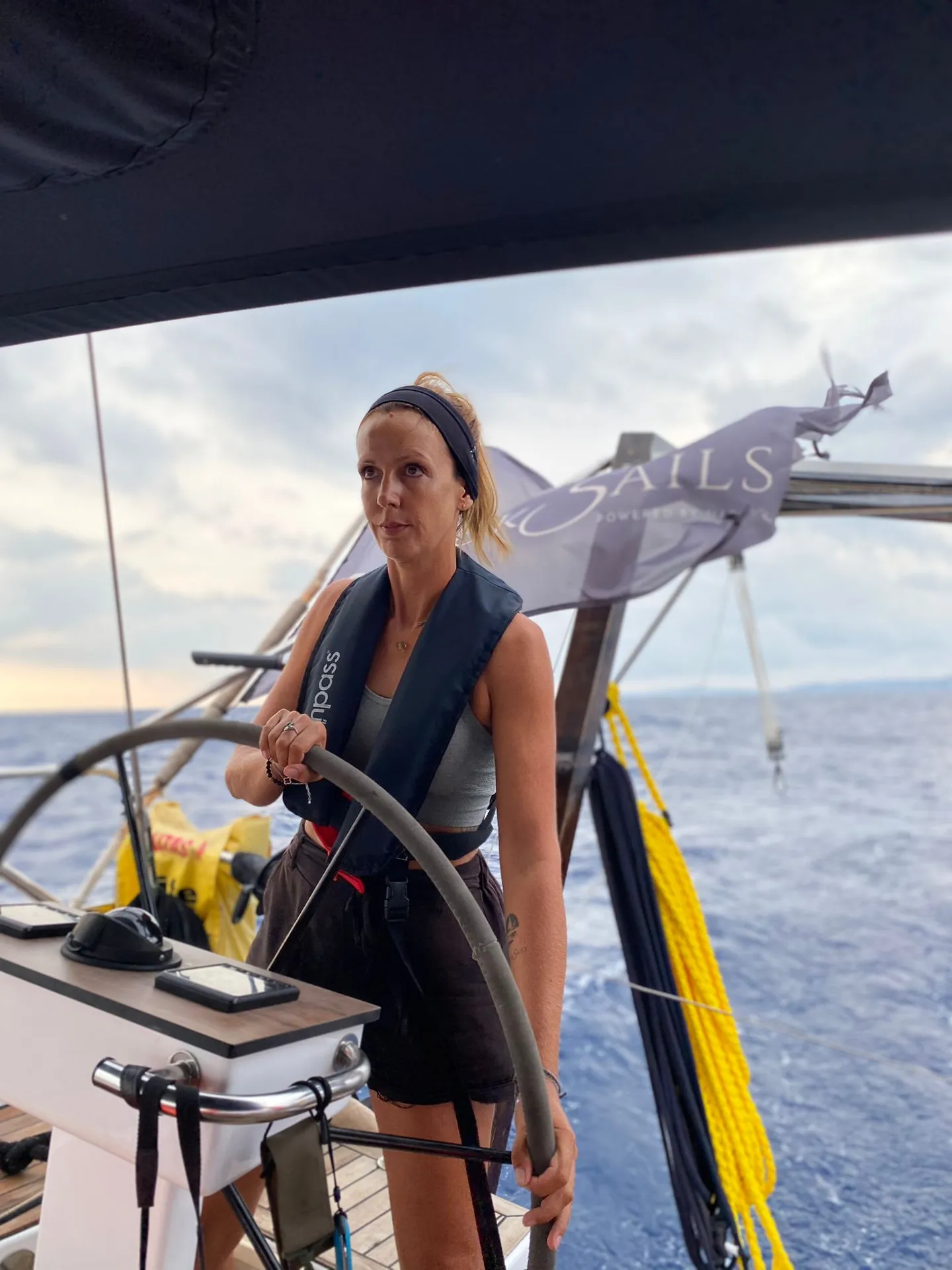 Eine Seglerin mit Rettungsweste am Steuerrad, dahinter die Black-Sails-Flagge