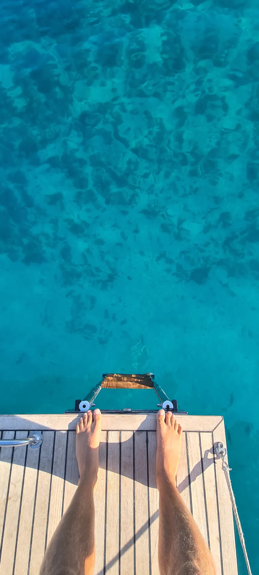 Füße auf der Badeplattform über türkisem Wasser