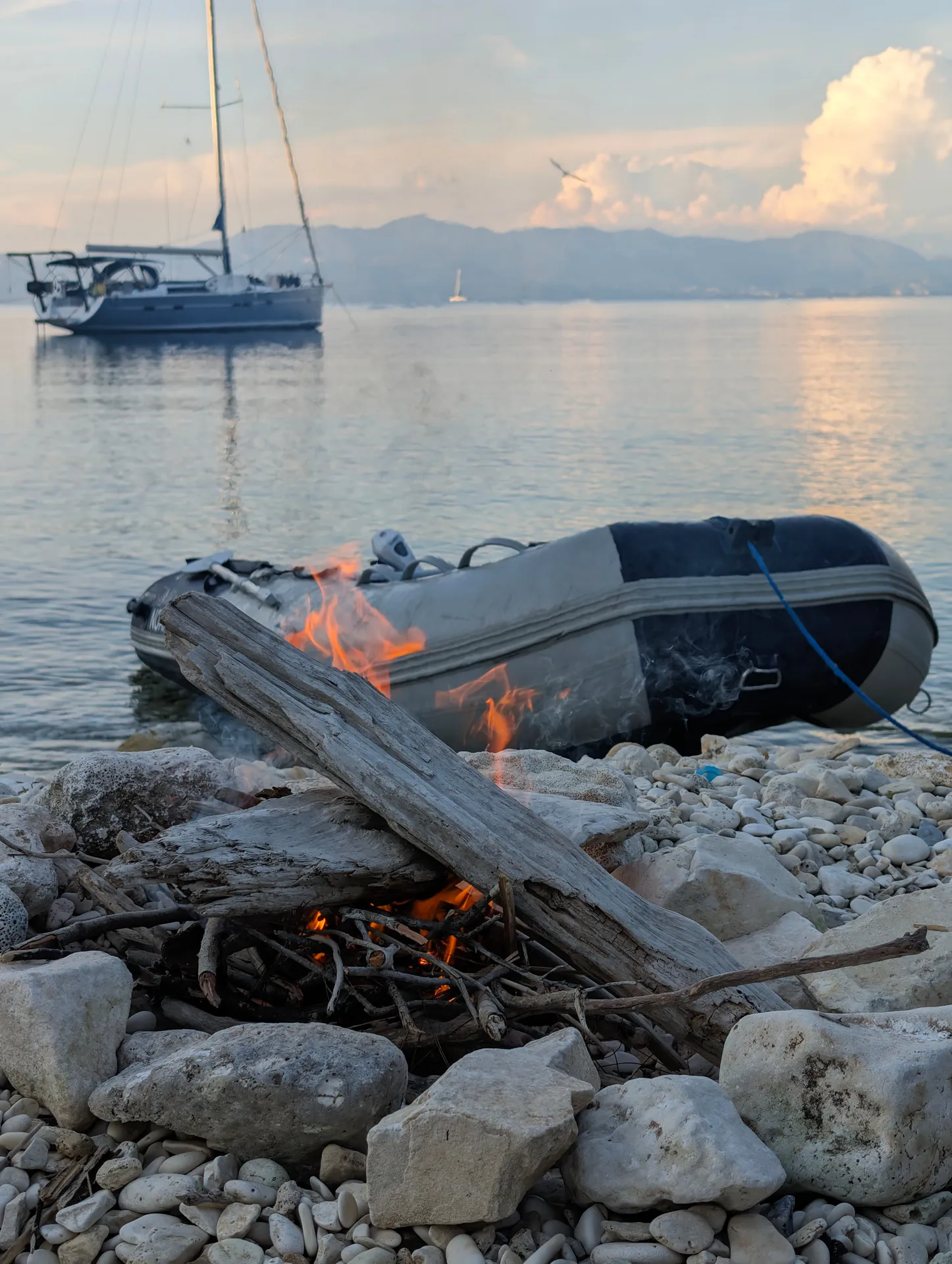 Lagerfeuer am Strand, Dinghi und Yacht vor Anker