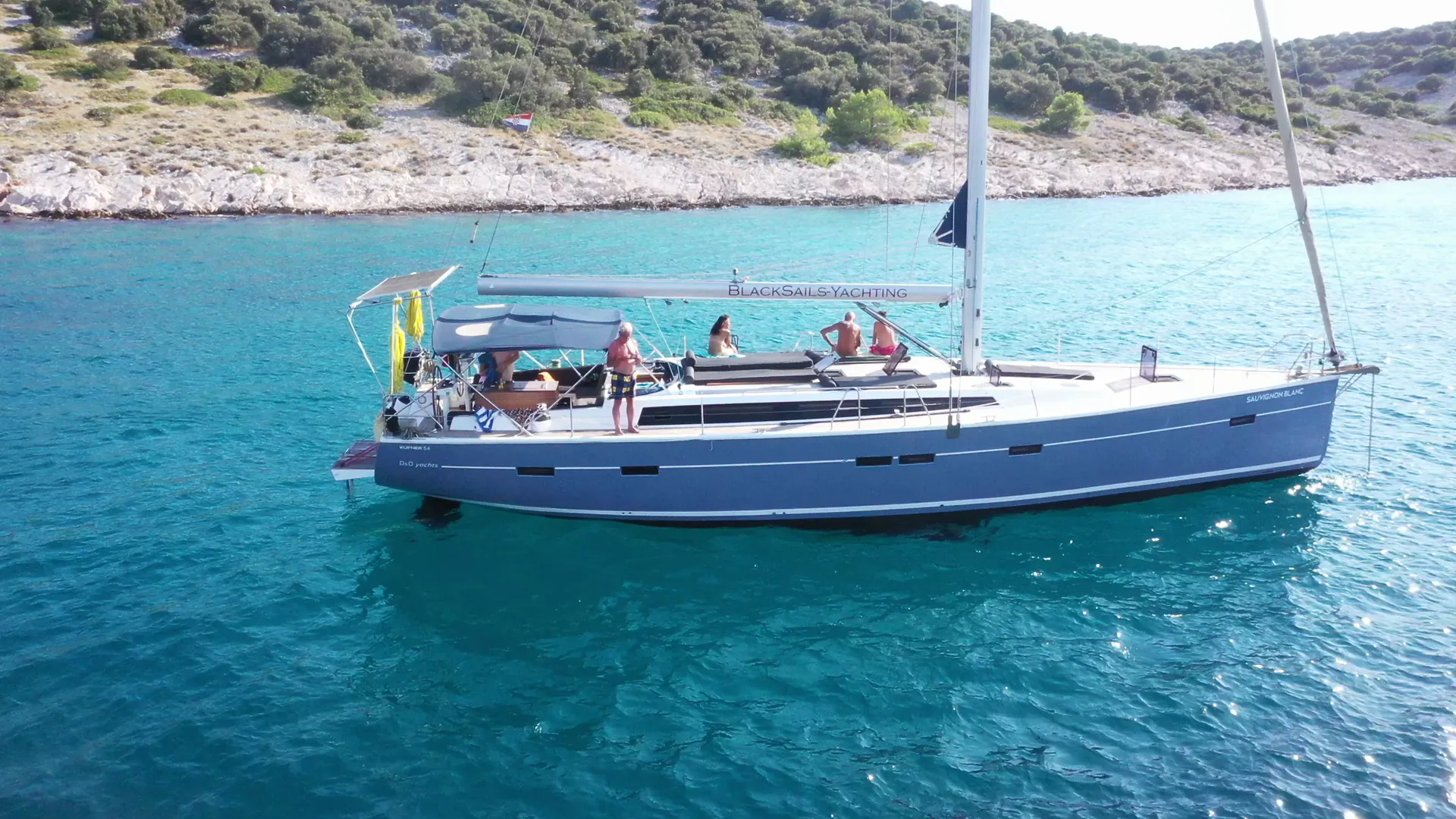 Die Sauvignon Blanc vor Anker in türkisem Wasser, Gäste an Deck, von der Seite aus der Luft