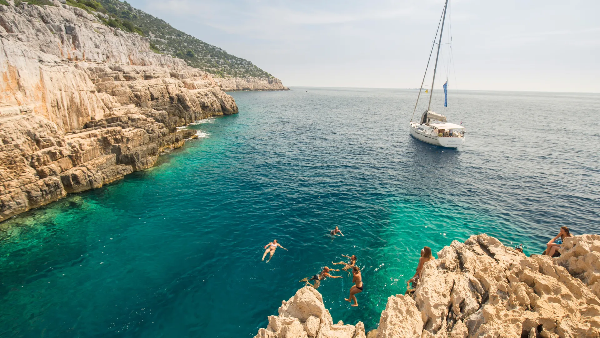 Ein Segelboot ankert in einer traumhaften Bucht in Kroatien, während die Crew das kristallklare Wasser genießt – das perfekte Erlebnis auf einem Mitsegeltörn.