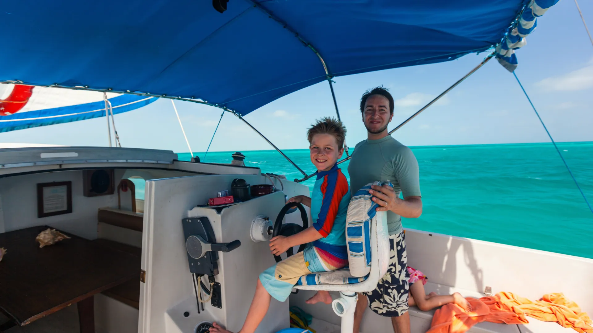 Ein erfahrener Skipper zeigt einem Kind das Steuern eines Segelboots beim Familienurlaub in Griechenland