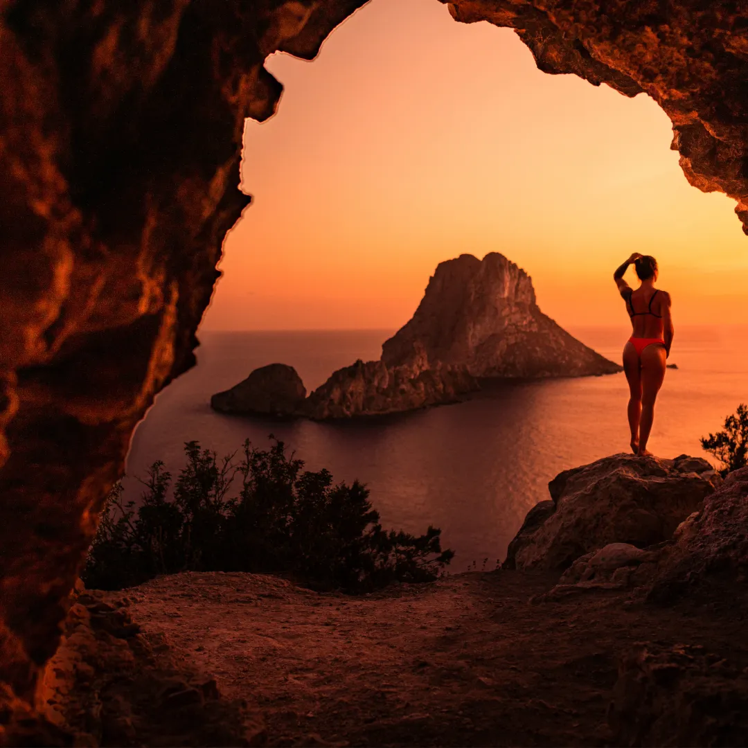 Frau betrachtet den Sonnenuntergang über der Insel Es Vedrà auf Ibiza – ein magischer Moment auf den Balearen, ideal für Segler und Naturfreunde
