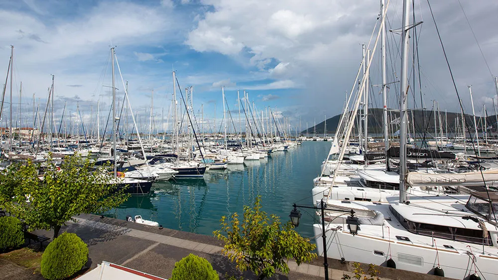 Levkas Marina im Ionischen Meer mit unzähligen Segelyachten und Katamaranen, umgeben von blauem Himmel, Wasser und grüner Promenade.