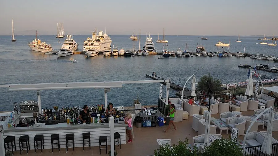 Luxusyachten und Segelboote in der NAOK Marina von Korfu-Stadt mit Bar und Lounge im Vordergrund bei Sonnenuntergang.