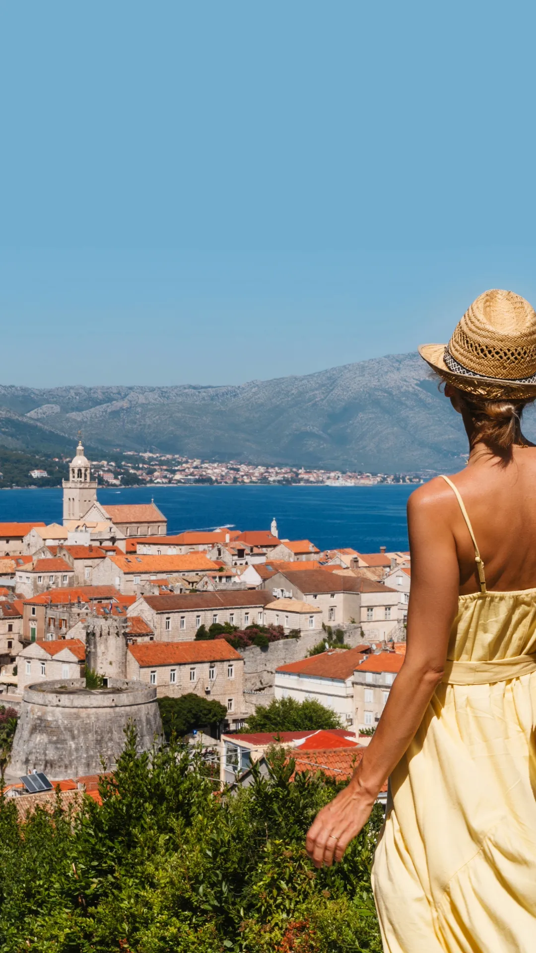 Frau mit Strohhut blickt auf die Altstadt von Korčula und das Meer – Symbol für Freiheit und Yachtcharter in Süddalmatien mit BlackSails-Yachting