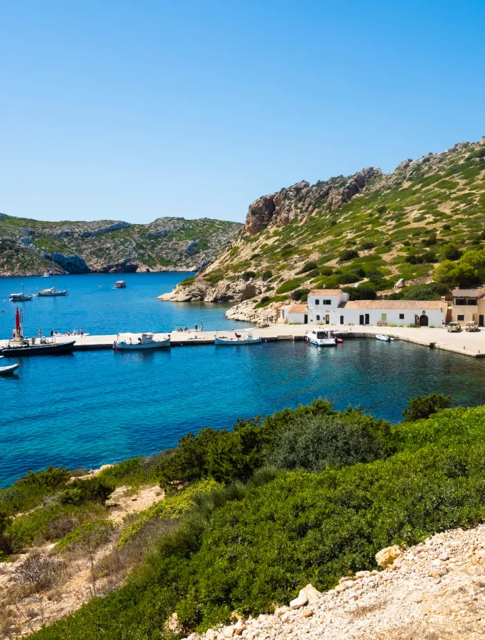 Blick auf den Hauptkai von Cabrera im Nationalpark mit Fischerhäusern, Anlegestelle und Segelbooten im Hintergrund – exklusives Segelziel mit BlackSails-Yachting.