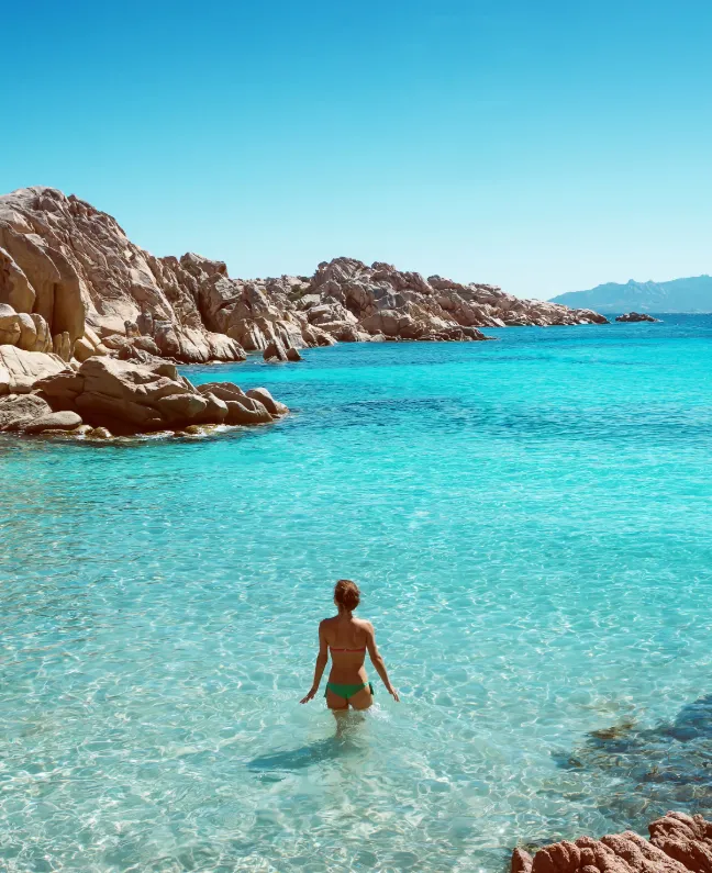 Frau steht im türkisblauen Wasser der Cala Coticcio auf Caprera – Traumbucht für Yachtcharter mit BlackSails-Yachting in Sardinien