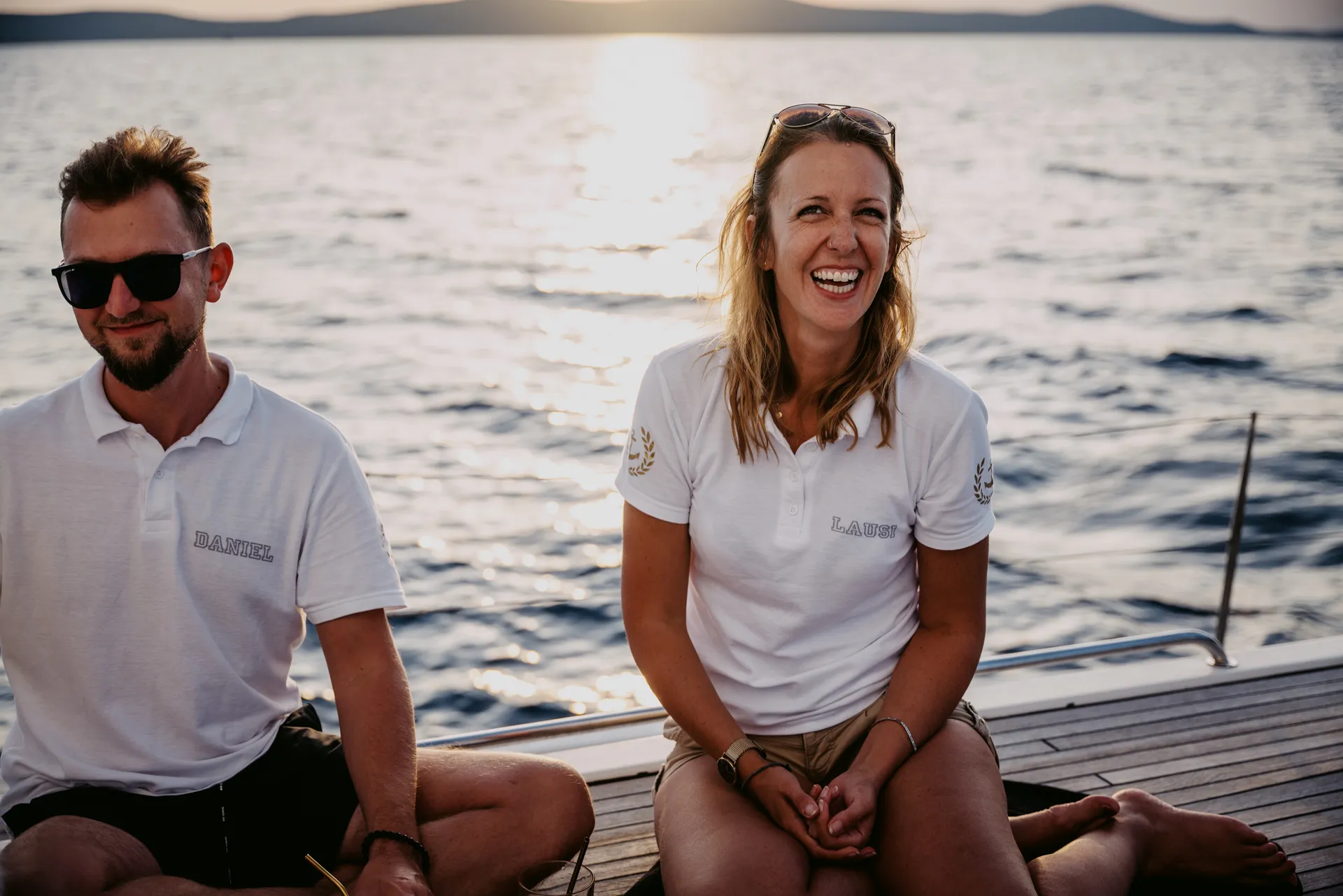 Laura und Daniel lächeln gemeinsam an Deck ihres Segelbootes nach einem erfolgreichen Törn
