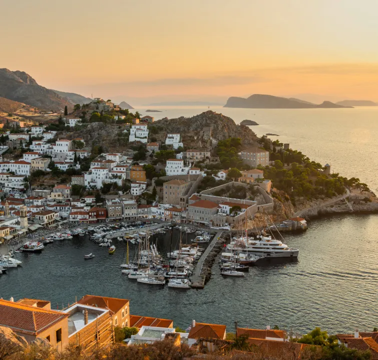 Abendstimmung über dem Hafen von Hydra mit weißen Häusern und festgemachten Yachten – ein Zwischenziel beim Yachtcharter mit BlackSails-Yachting