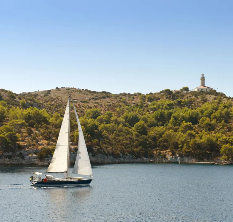 Segelyacht vor der Küste von Lastovo mit Leuchtturm auf dem Hügel – abgeschiedener Naturspot beim Yachtcharter Süddalmatien mit BlackSails-Yachting