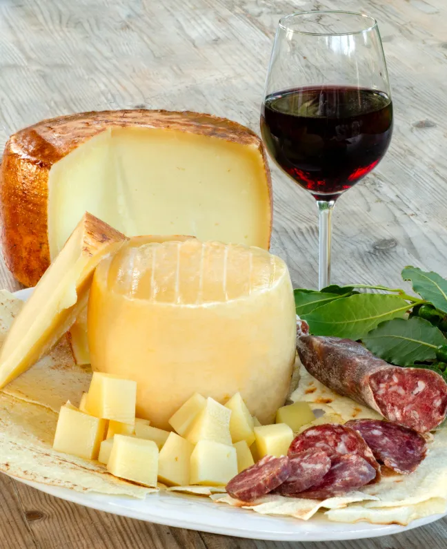 Sardischer Käse, Salami und ein Glas Rotwein auf Holzplatte – kulinarischer Auftakt einer Yachtcharter mit BlackSails-Yachting ab Portisco