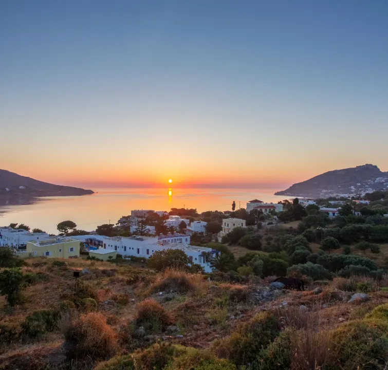Sonnenaufgang über einem Küstenort der Sporaden mit Blick auf ruhiges Meer, Inselhügel und typische weiße Häuser.