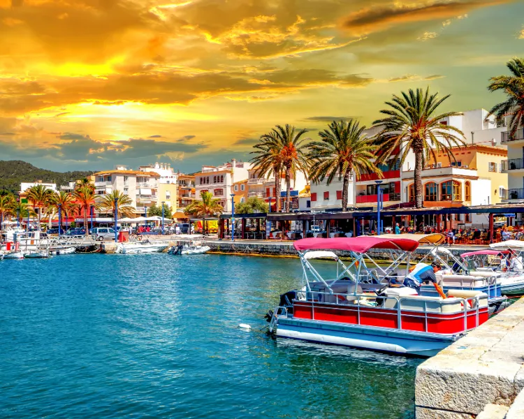 Blick auf die Hafenpromenade von Port d’Andratx bei Sonnenuntergang mit Booten, Palmen und Restaurants