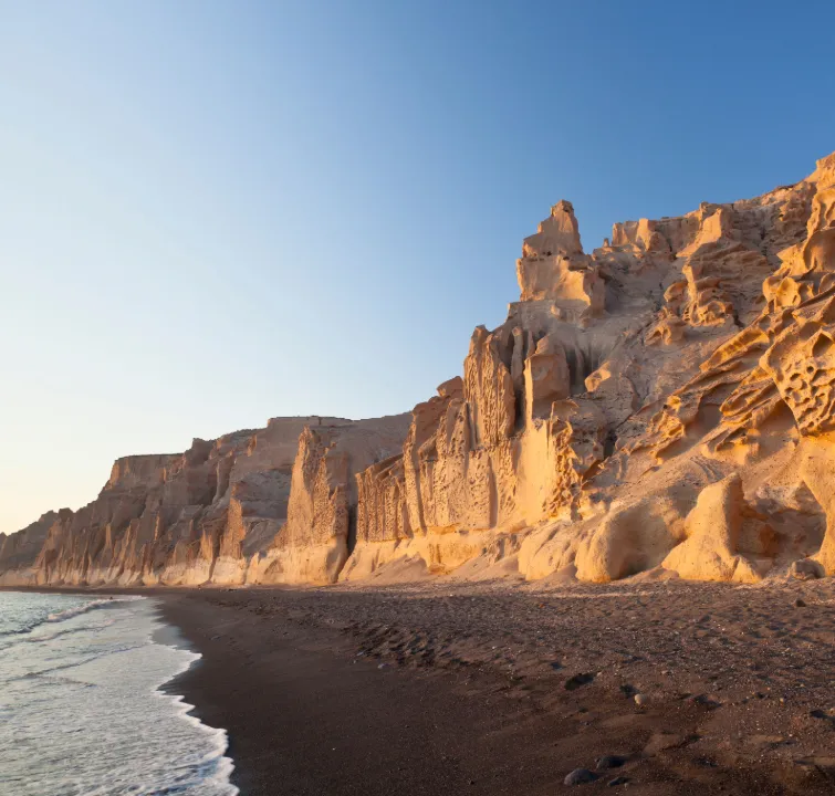 Sonnenbeschienene Felsformationen und schwarzer Sandstrand an einer abgelegenen Küste im Dodekanes – ein Naturhighlight auf einer Yachtcharter mit BlackSails-Yachting.