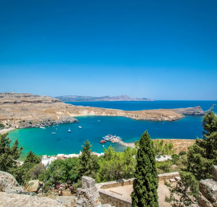 Blick auf eine Bucht im Dodekanes mit Segelyachten vor Anker – ideal für Yachtcharter mit BlackSails-Yachting: türkisblaues Wasser, geschützte Lage und wilde Küstenlandschaft zwischen Kos und Rhodos.