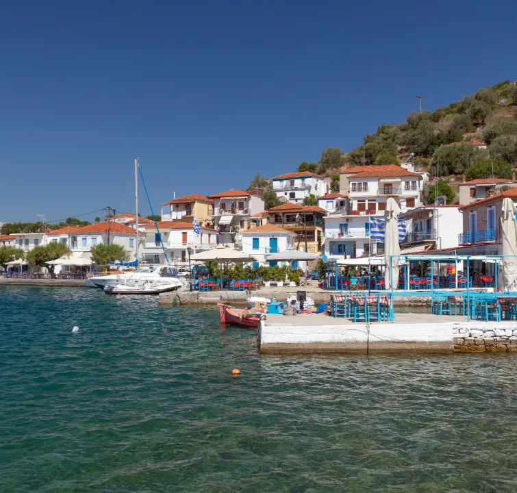 Küstenort in Griechenland mit weiß-blauen Häusern, Tavernen und anliegenden Yachten – idealer Zwischenstopp beim Yachtcharter mit BlackSails-Yachting.