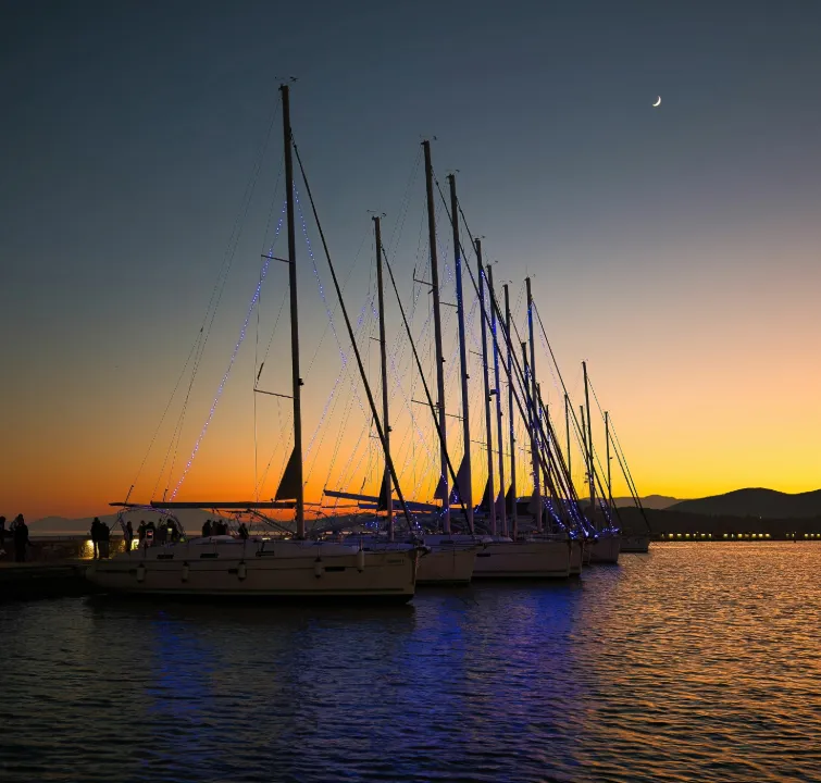 Yachten bei Sonnenuntergang mit Lichtinstallationen am Mast, ruhiger Hafen, Abendstimmung – Start oder Rückkehr beim Yachtcharter mit BlackSails-Yachting.