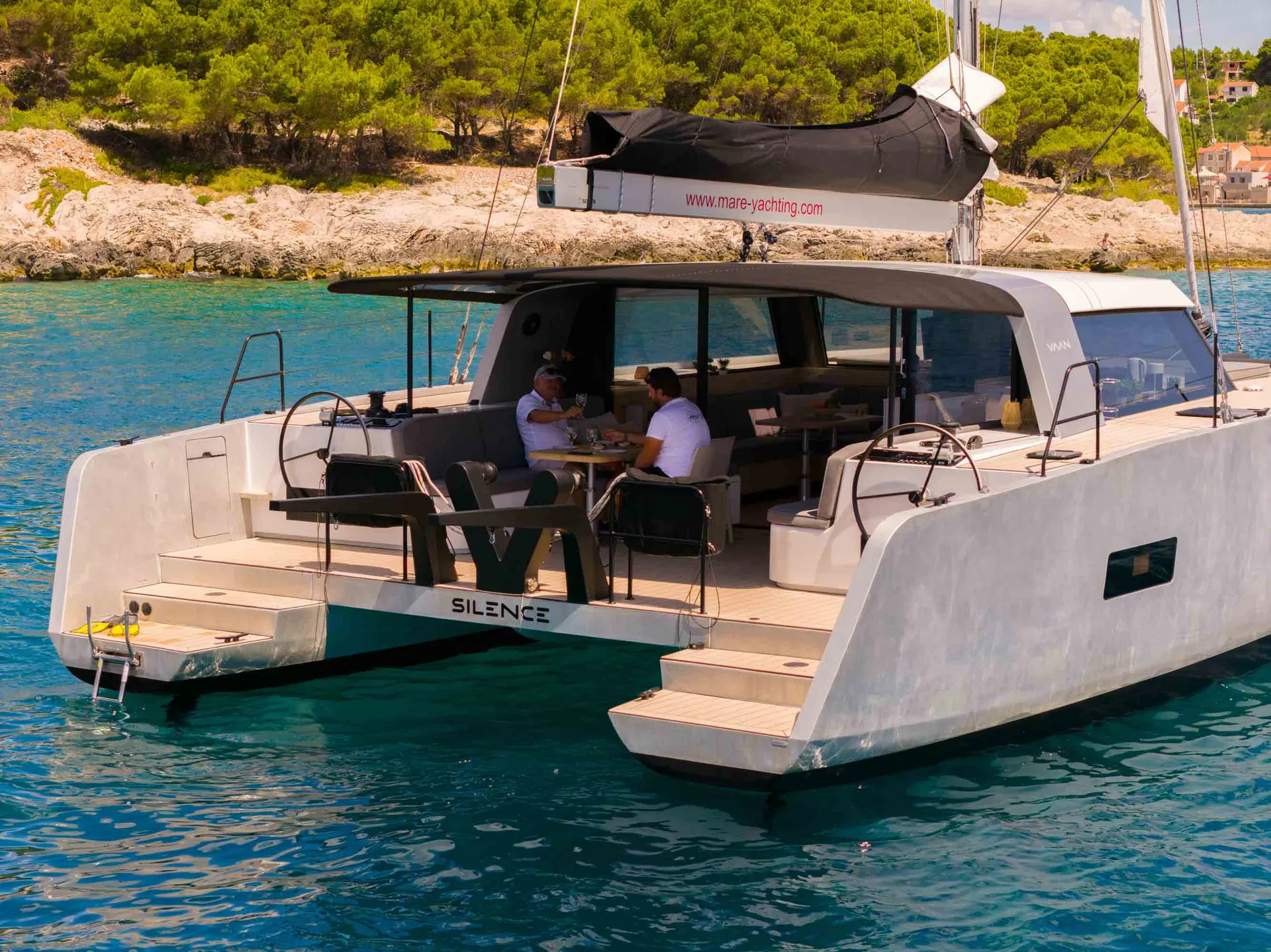 VAAN R4 Silence – Rückansicht eines vollelektrischen Katamarans mit offener Terrasse und zwei Personen beim Essen an Bord, vor Anker in Kroatien.